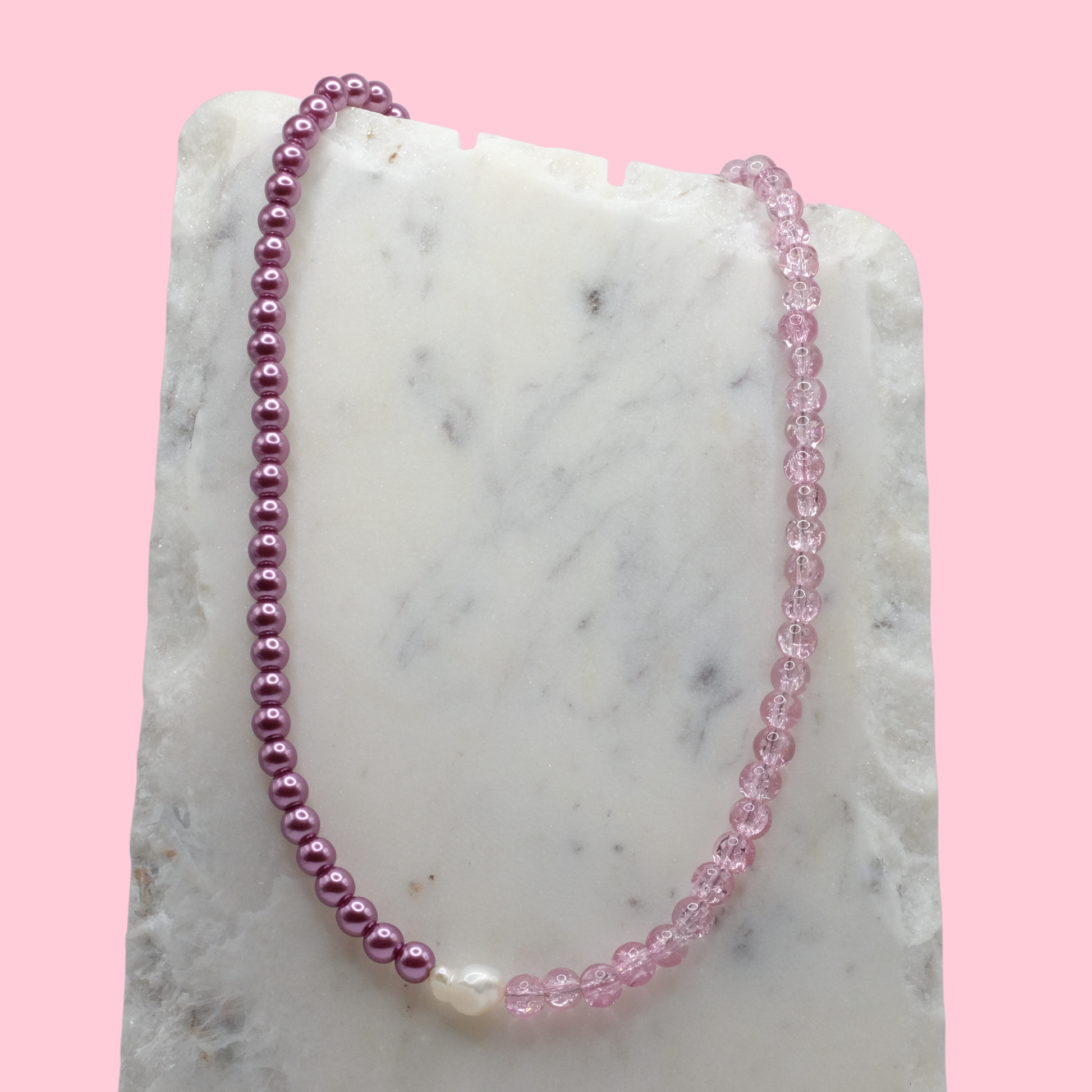 Necklace with pink and purple beads on a marble surface with a pink background