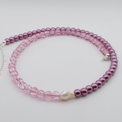 A handmade beaded necklace composed of 6mm metallic plum glass beads on one side and 6mm mauve crackle glass beads on the other, featuring a freshwater pearl centrepiece, displayed on a white background.