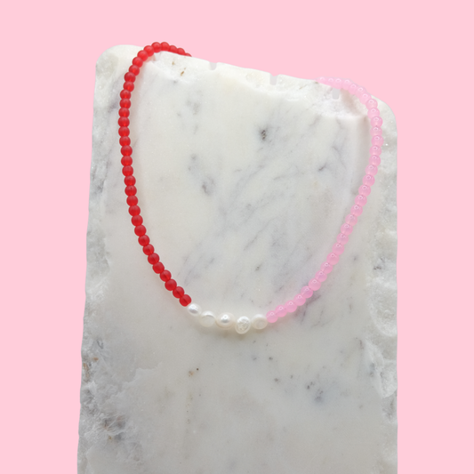 Necklace with red and pink beads on a marble surface with a pink background