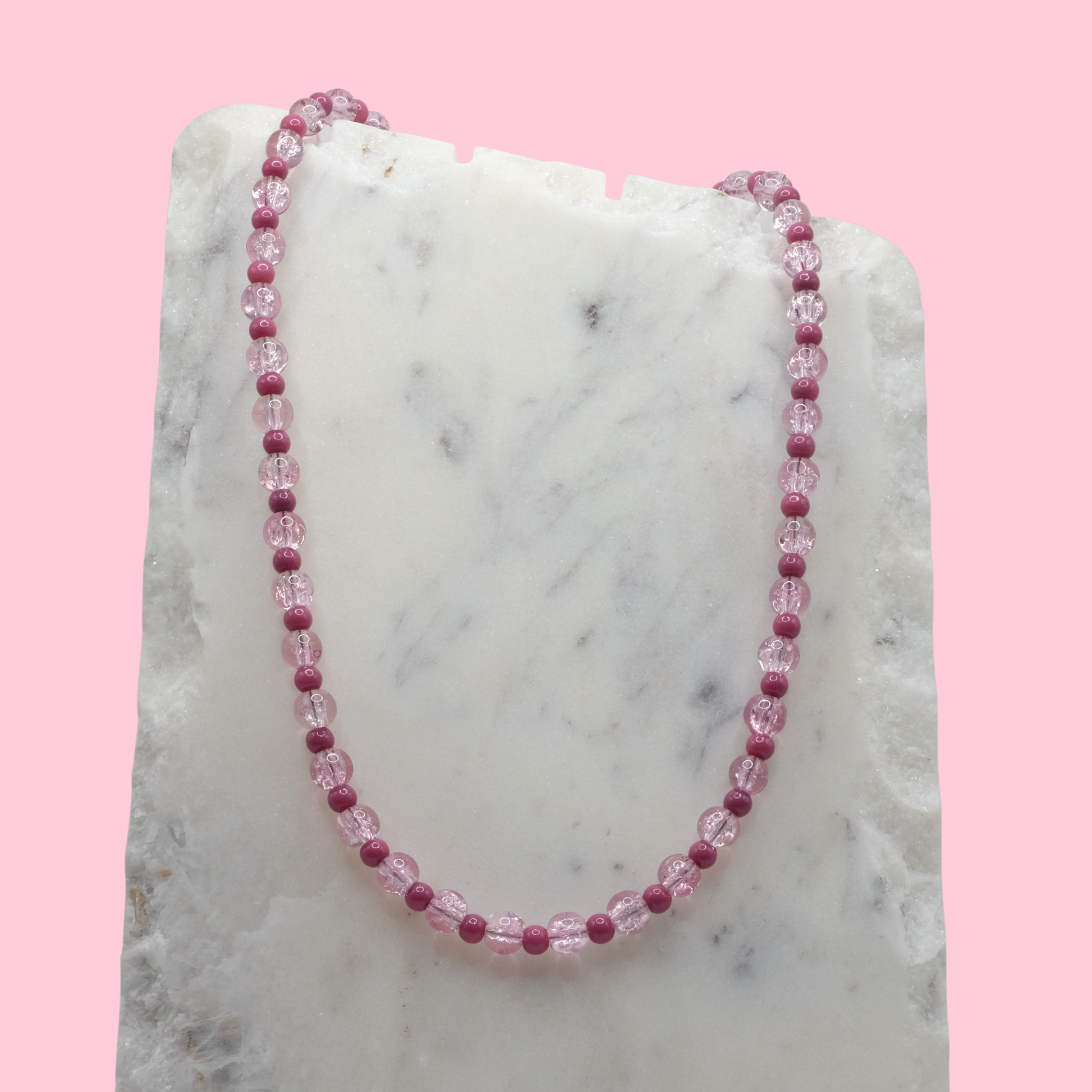 Necklace with pink beads on a marble surface with a pink background