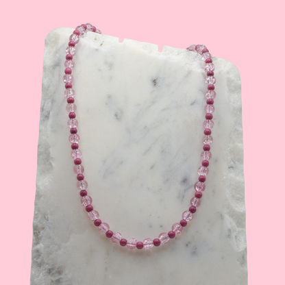 Necklace with pink beads on a marble surface with a pink background