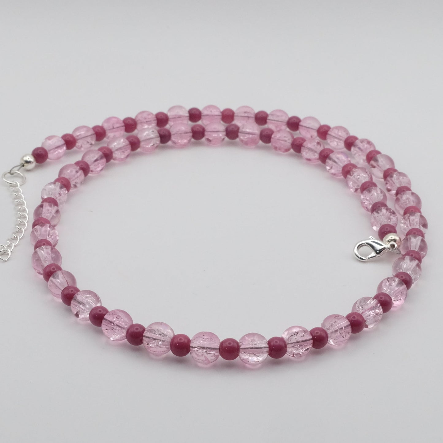 A handmade beaded necklace featuring alternating 6mm and 4mm pink crackle glass and rose pink glass beads, displayed on a white marble jewellery stand.