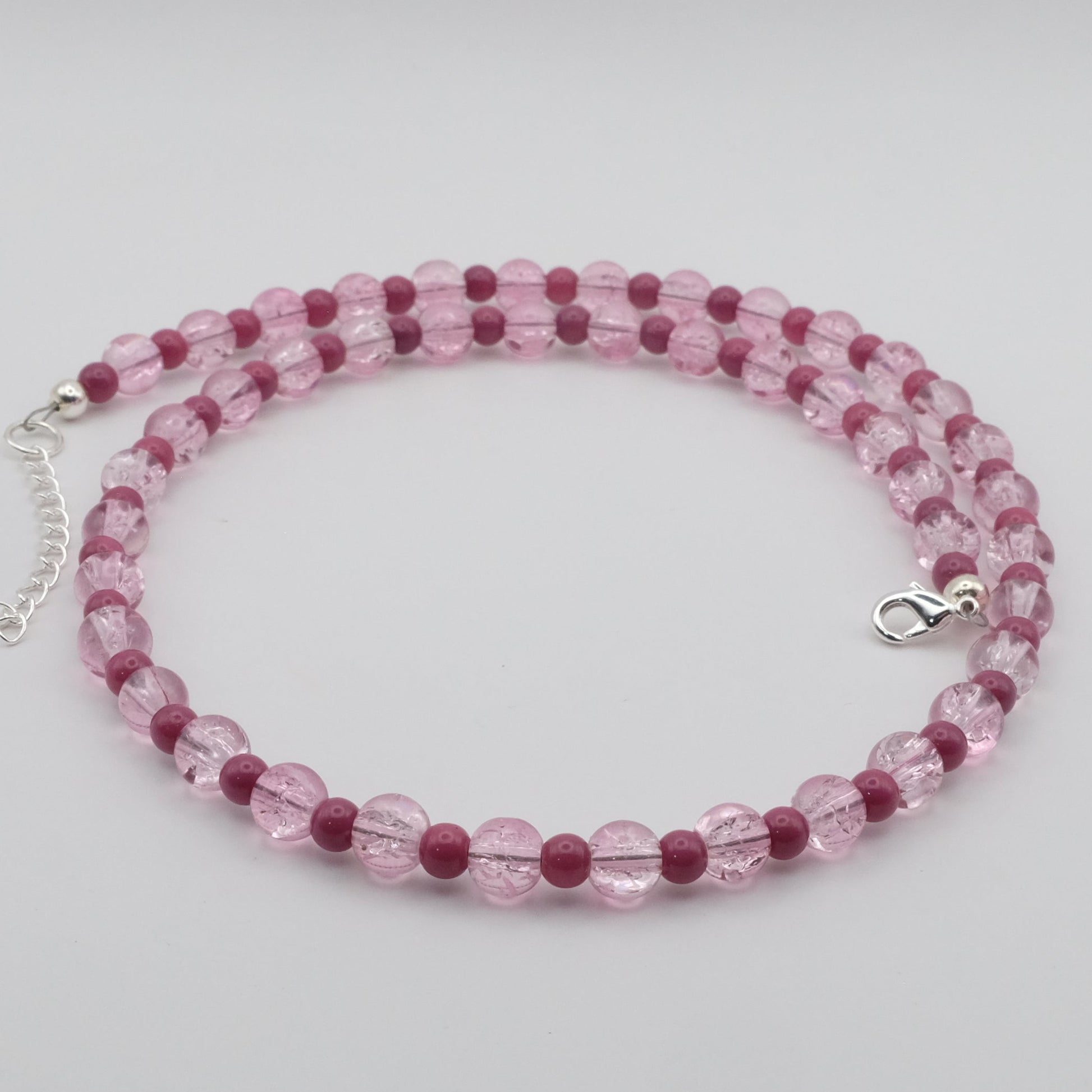 A handmade beaded necklace featuring alternating 6mm and 4mm pink crackle glass and rose pink glass beads, displayed on a white marble jewellery stand.