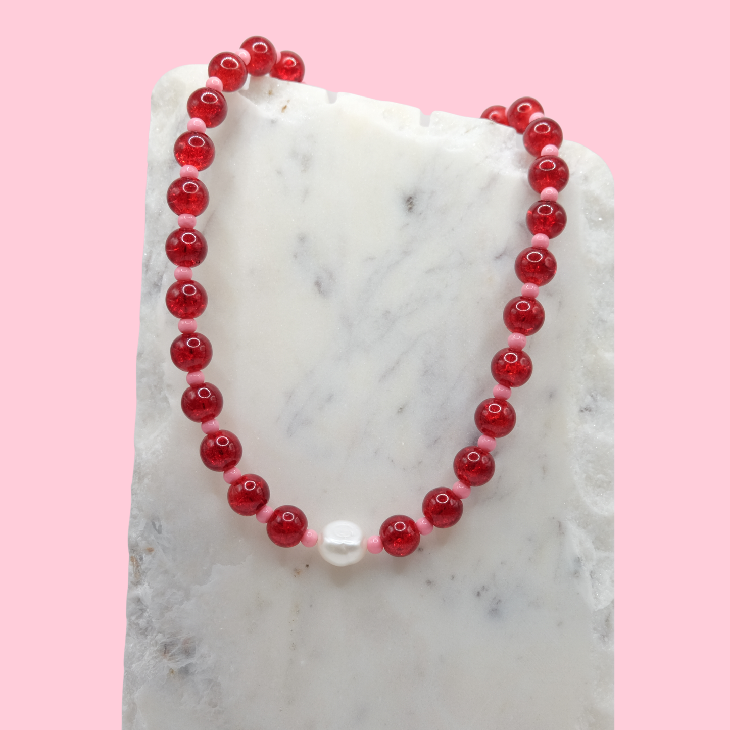 Red beaded necklace with a white pearl on a marble surface with a pink background