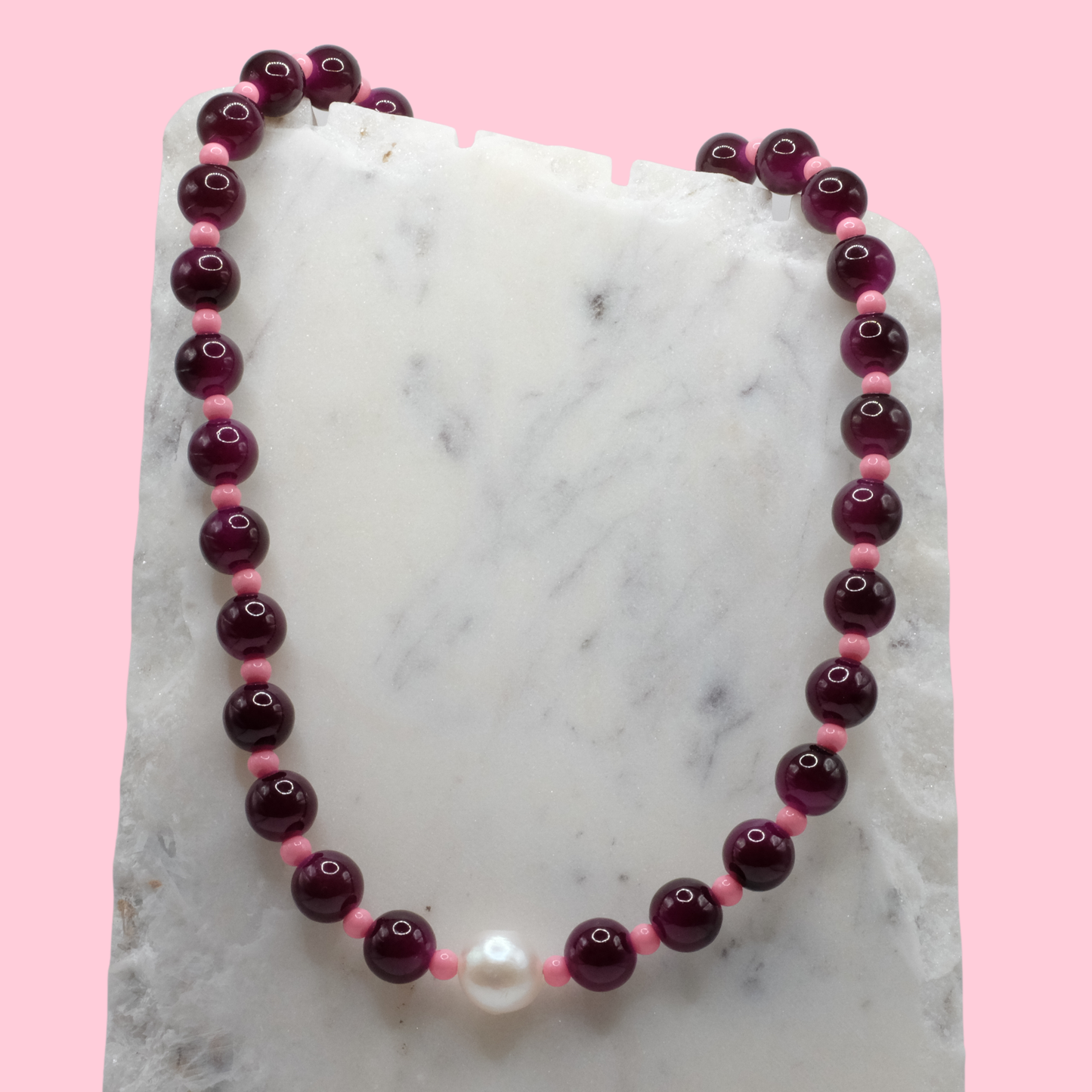 Beaded necklace with purple and pink beads on a marble surface with a pink background