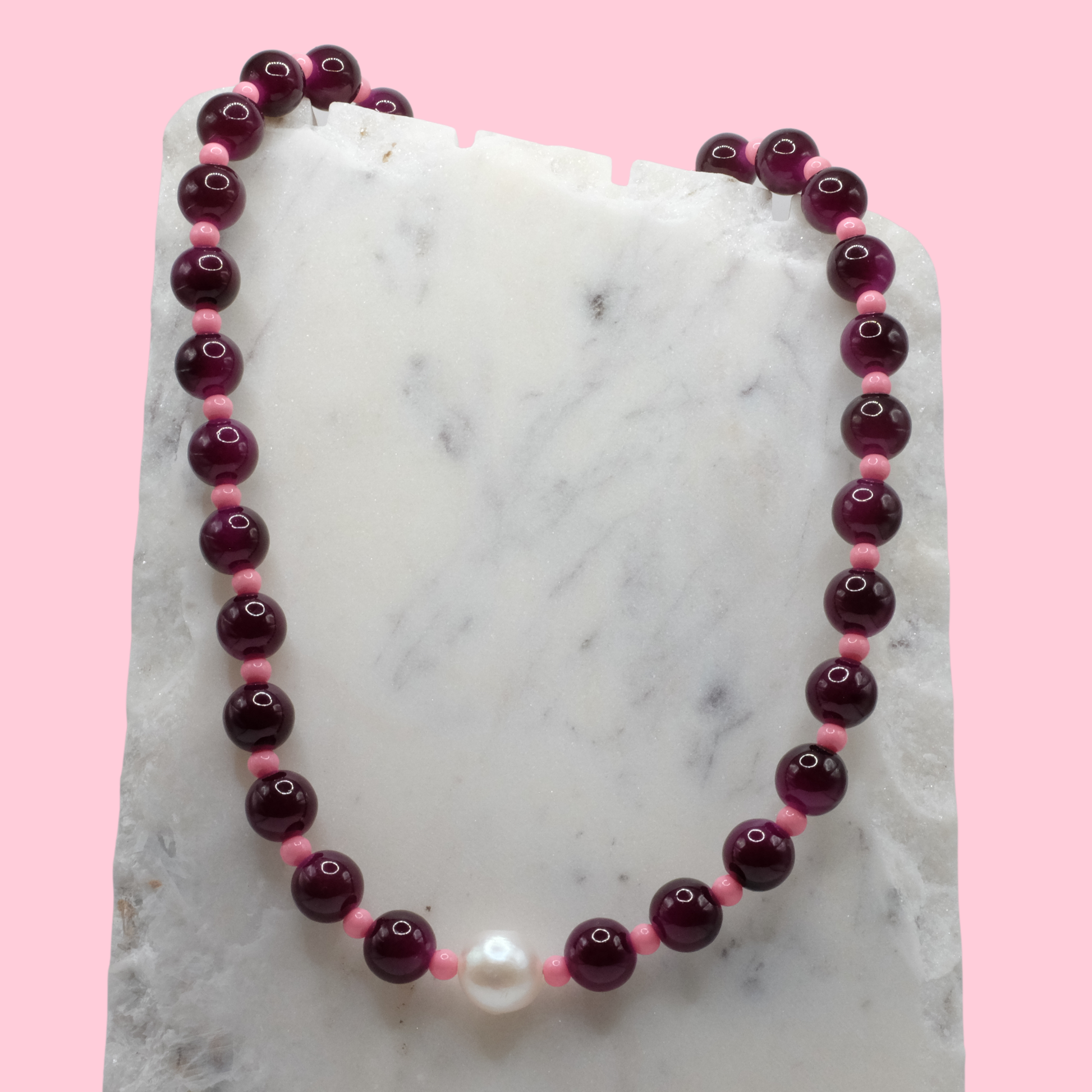 Beaded necklace with purple and pink beads on a marble surface with a pink background