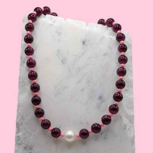 Beaded necklace with purple and pink beads on a marble surface with a pink background