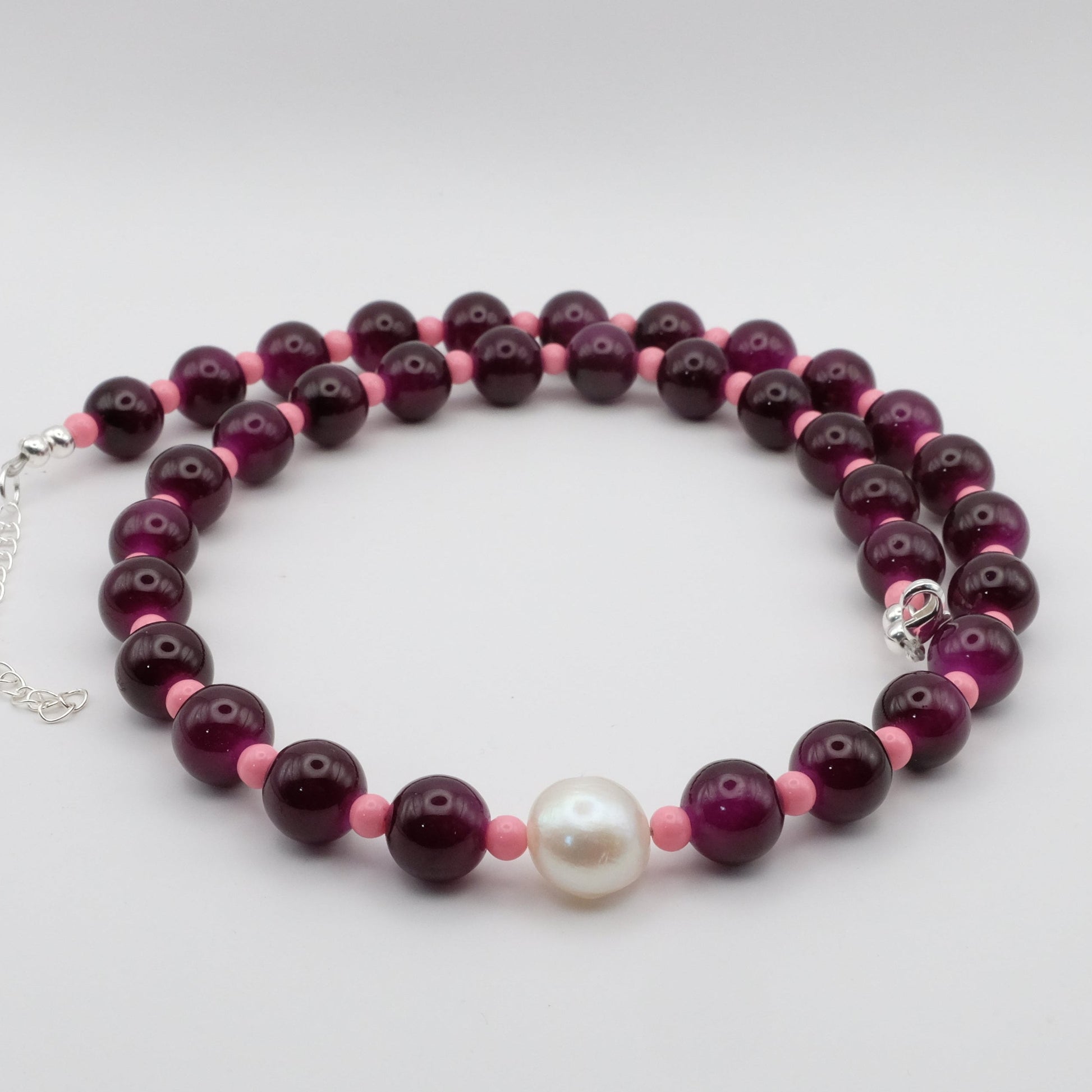 Necklace with purple and pink beads and a white pearl on a light gray background