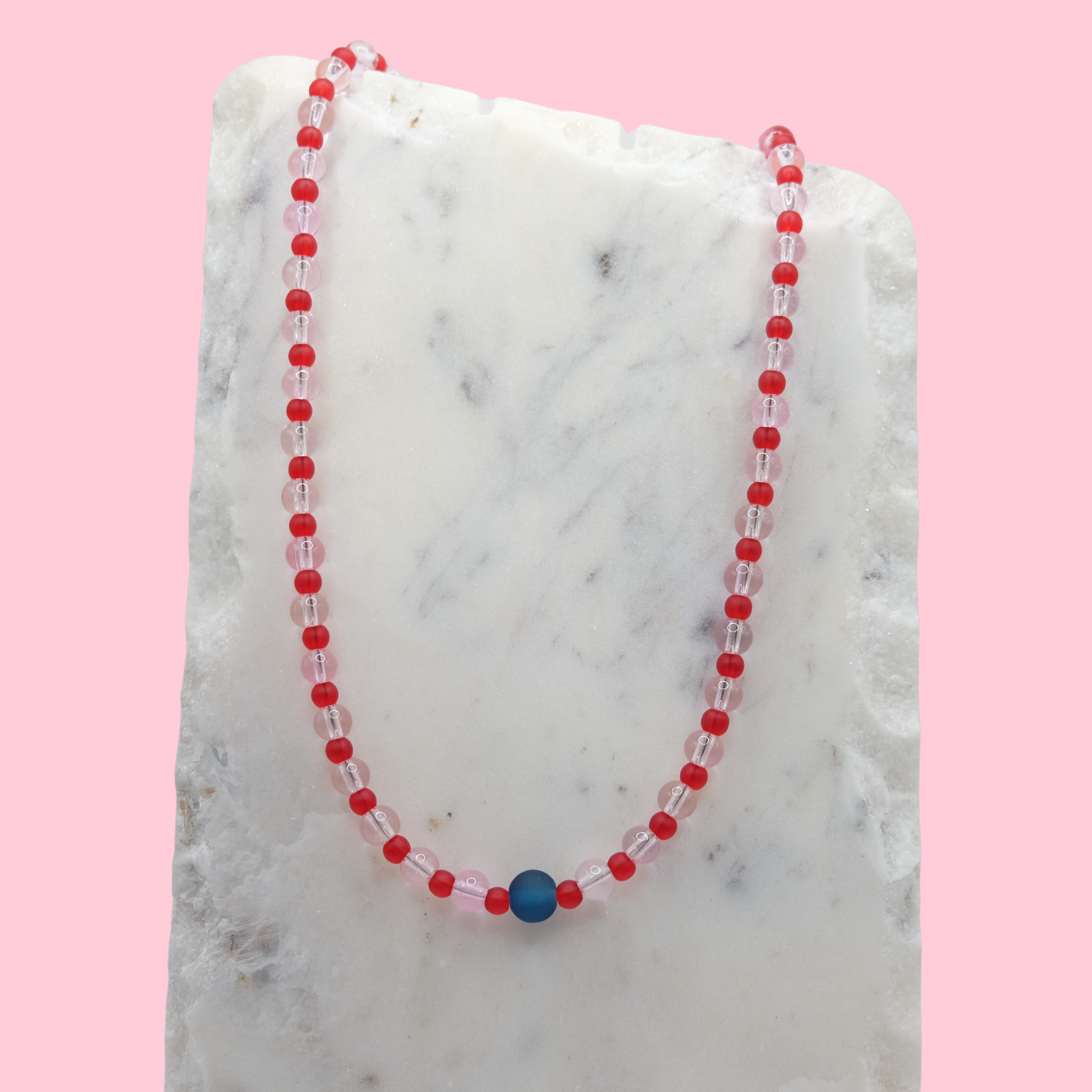Necklace with red and clear pink beads on a marble surface with pink background