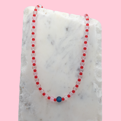 Necklace with red and clear pink beads on a marble surface with pink background