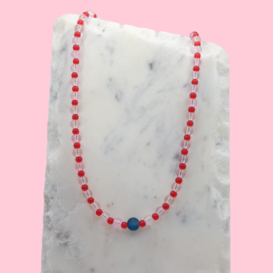 Necklace with red and clear pink beads on a marble surface with pink background
