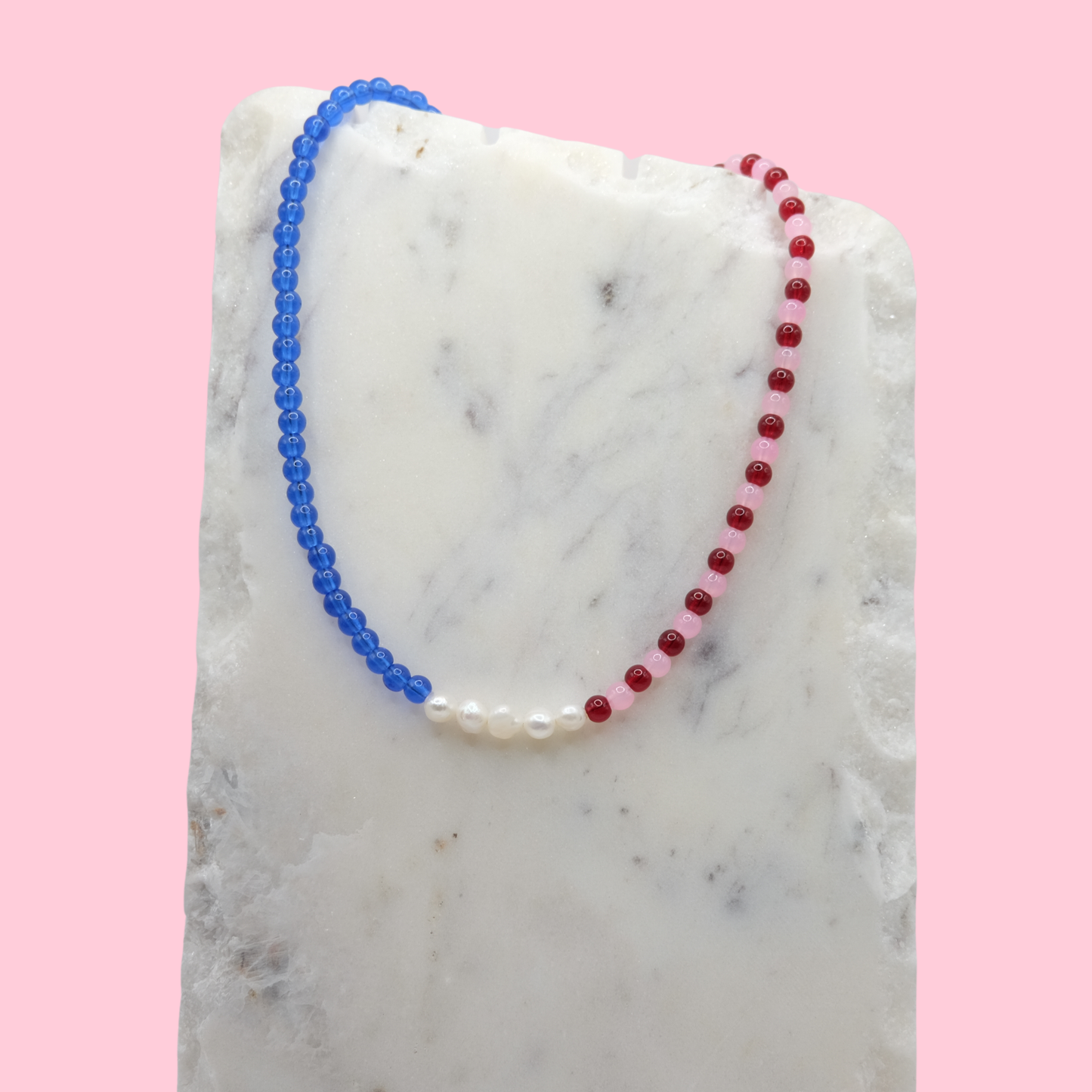 Necklace with blue and red beads on a marble surface with a pink background