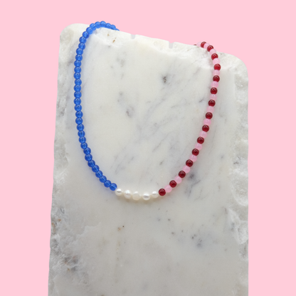 Necklace with blue and red beads on a marble surface with a pink background