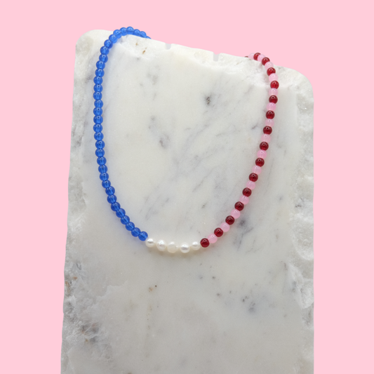 Necklace with blue and red beads on a marble surface with a pink background
