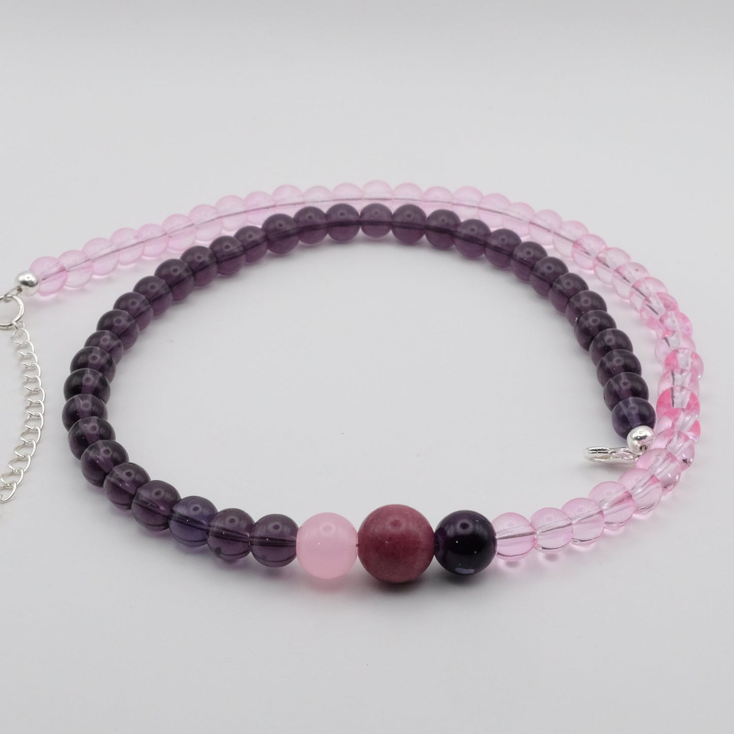 A handmade beaded necklace composed of 6mm light pink glass beads on one side and 6mm deep plum glass beads on the other, featuring pink, plum and deep purple glass bead accents at the centre, displayed on a white background.