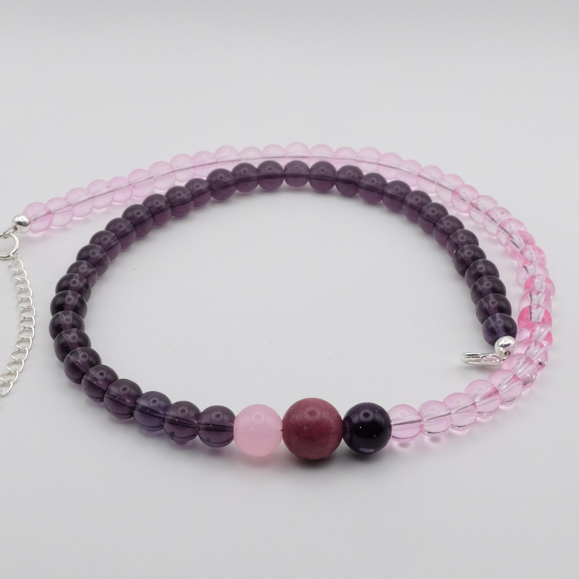 A handmade beaded necklace composed of 6mm light pink glass beads on one side and 6mm deep plum glass beads on the other, featuring pink, plum and deep purple glass bead accents at the centre, displayed on a white background.