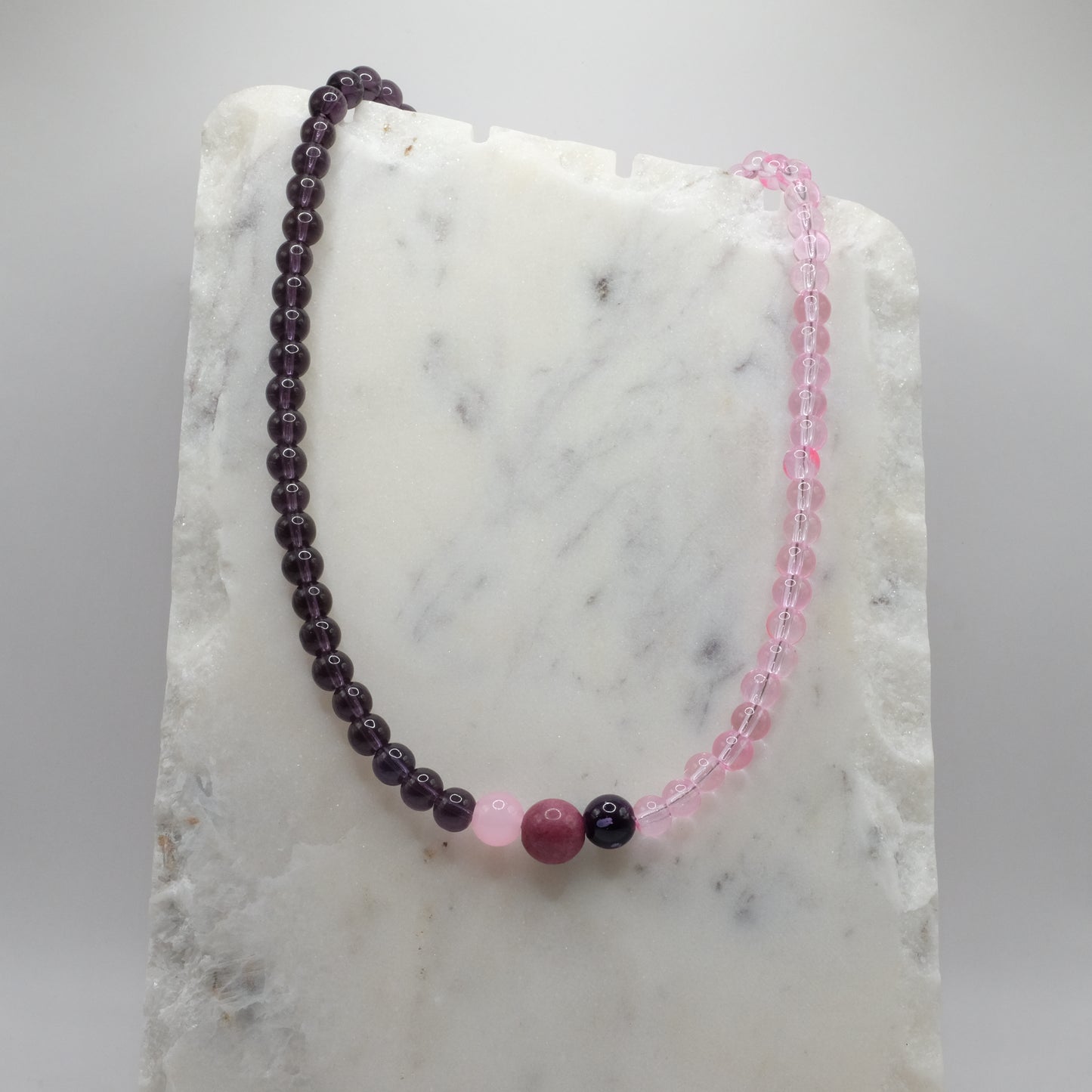Two beaded bracelets, one purple and one pink, on a marble surface.