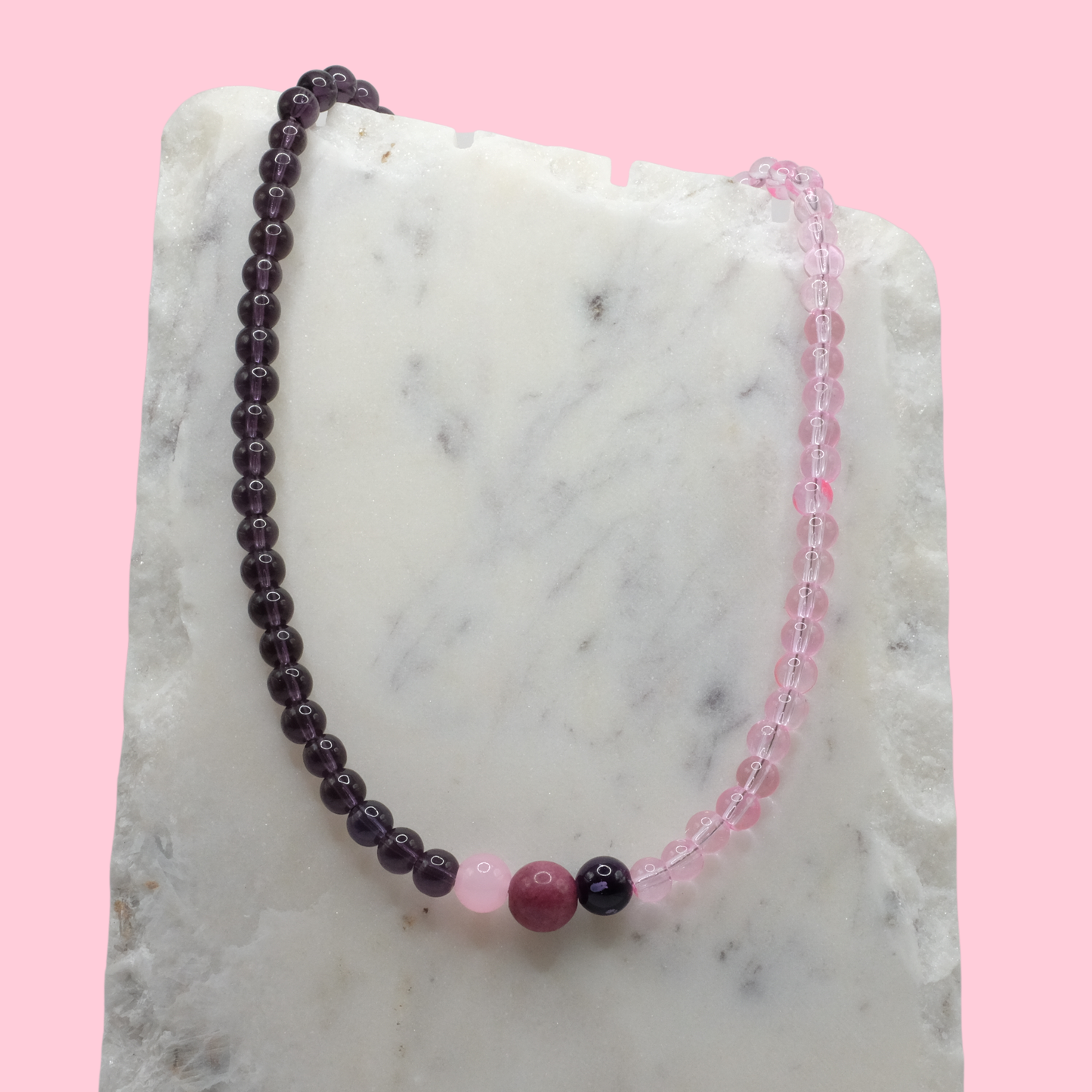Beaded necklace with purple and pink beads on a marble surface with a pink background