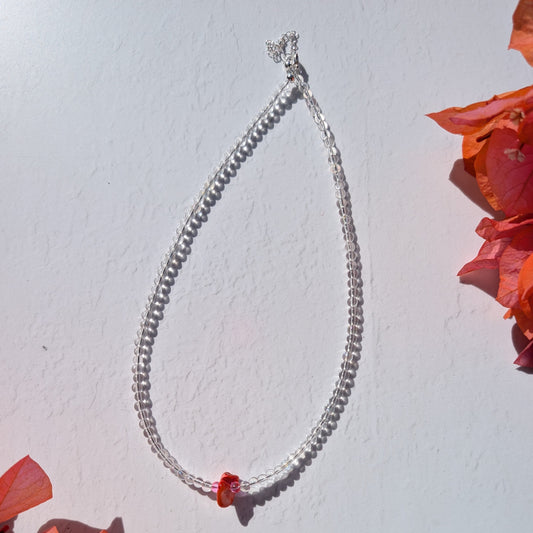 Minimal handmade beaded necklace with clear glass beads and a small orange shell chip centre detail accented with pink glass.