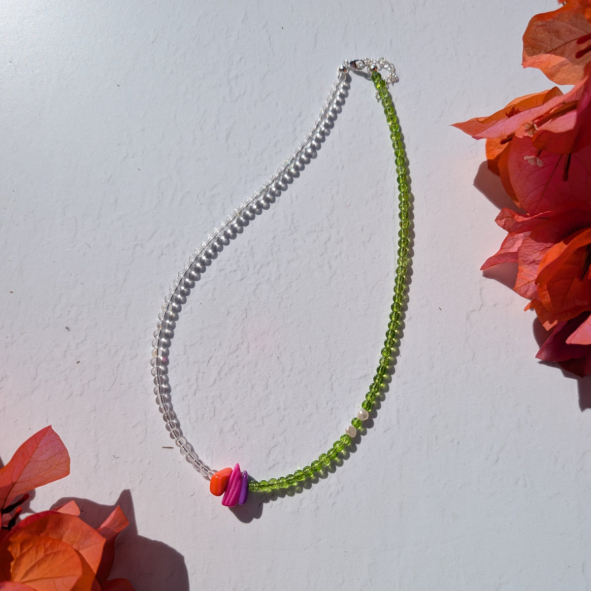 Asymmetric handmade necklace with clear and green glass beads, colourful shell chip accents and two freshwater pearls.