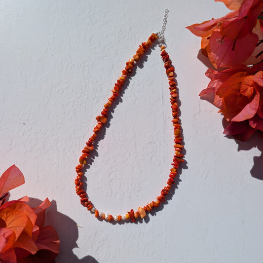 Alt image text: Handmade orange beaded necklace with irregular coral chip beads and freshwater pearl details, styled in sunlight with bougainvillea.
