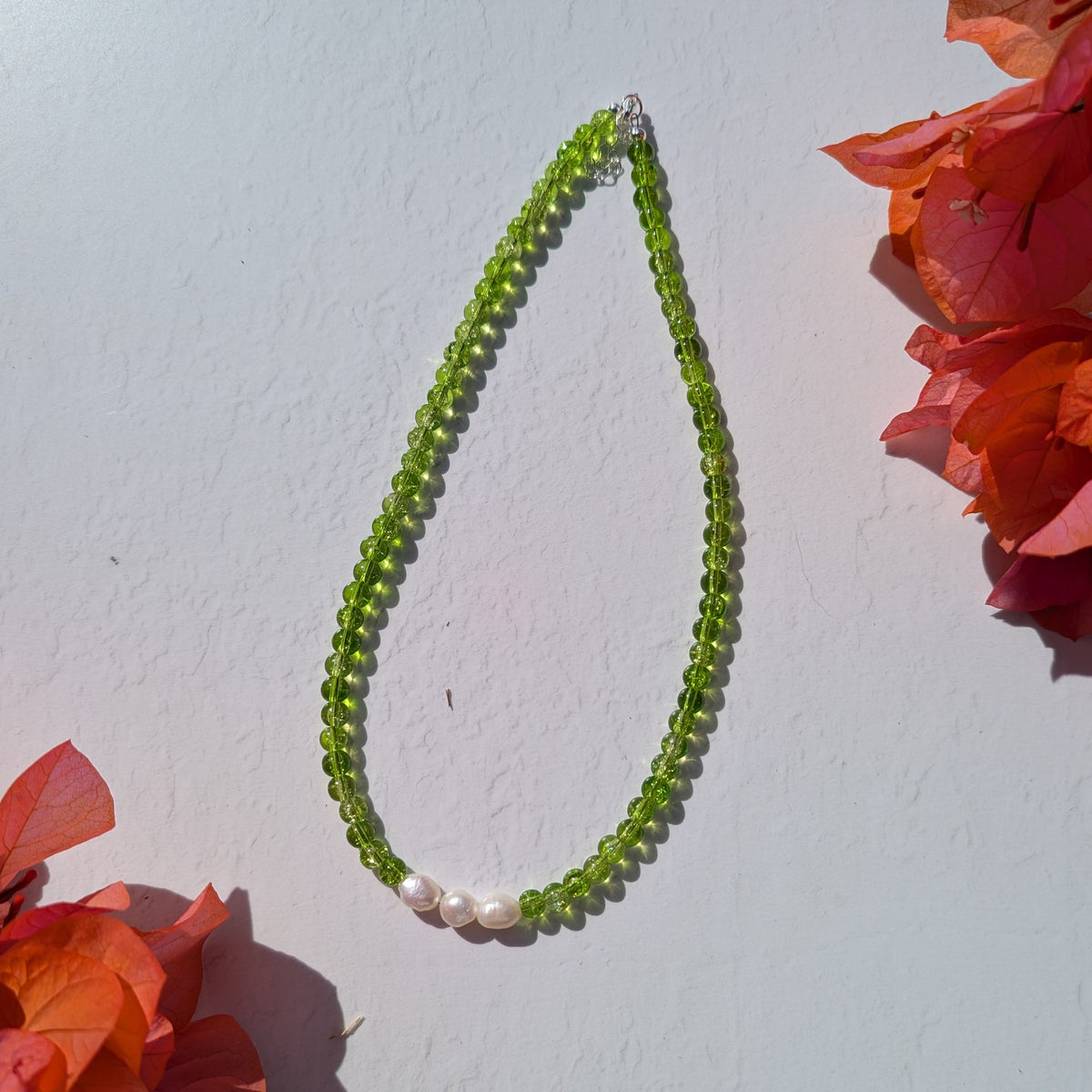 Handmade green beaded necklace with translucent green glass beads and three freshwater pearls, photographed in bright natural light.