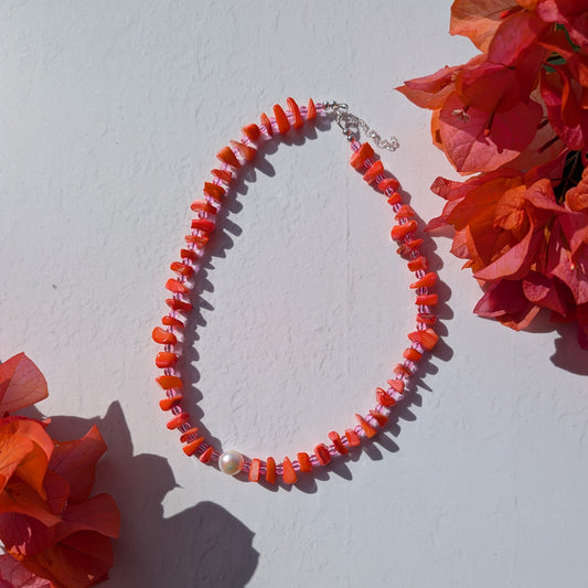 Handmade beaded necklace with orange shell chip beads, pink glass beads and a single freshwater pearl, photographed with bougainvillea.