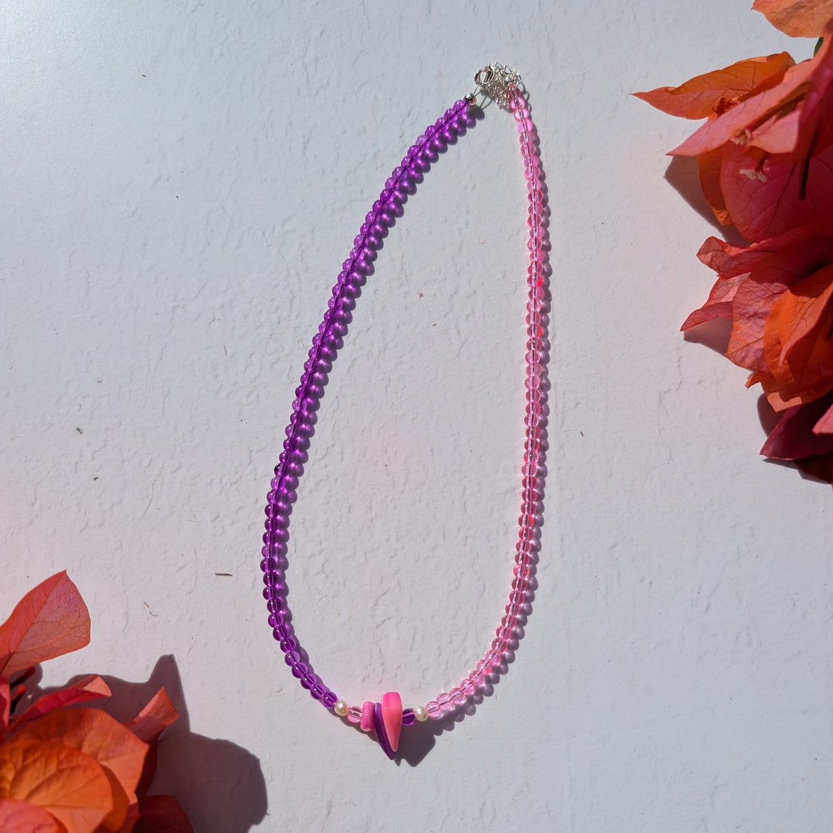 Handmade two-tone glass bead necklace in purple and pink with shell chip beads and small freshwater pearl accents at the centre.
