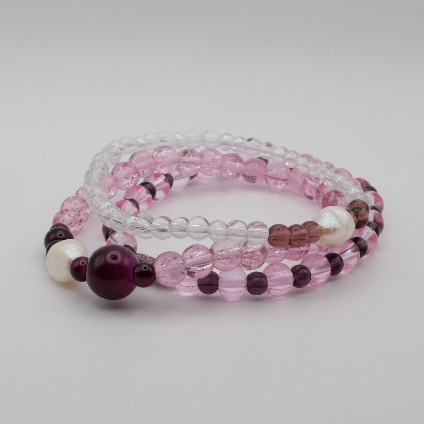 Set of three beaded bracelets with pink, purple, and clear beads on a light gray background