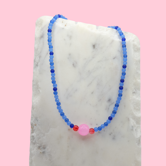 Beaded necklace with blue and pink beads on a marble surface with a pink background