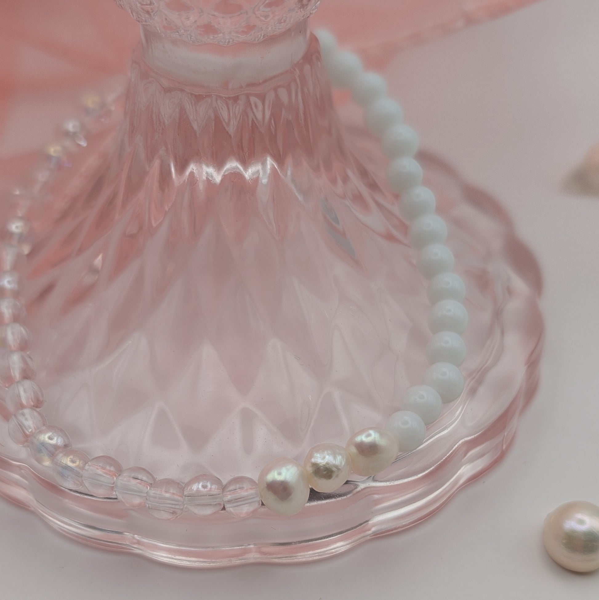 Pearl bracelet on a pink glass stand with scattered pearls on a light pink background