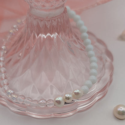 Pearl bracelet on a pink glass stand with scattered pearls on a light pink background