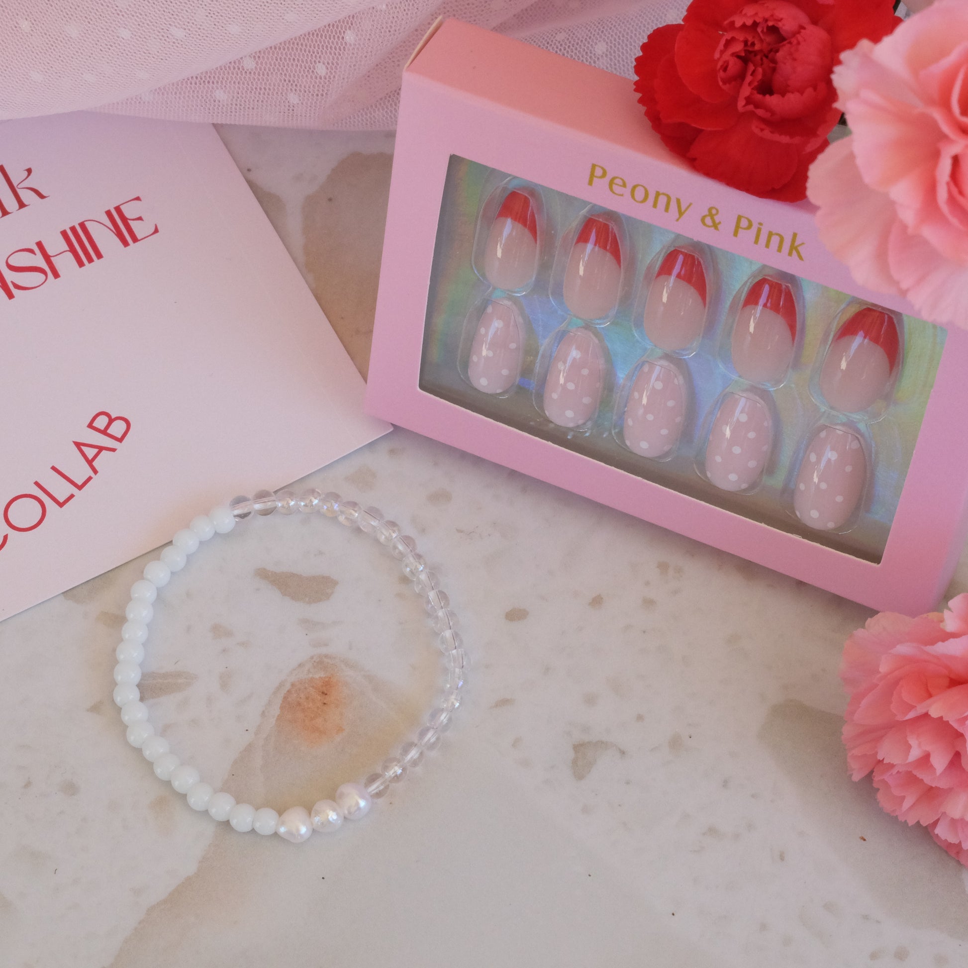 Pink box with false nails, bracelet, and flowers on a marble surface