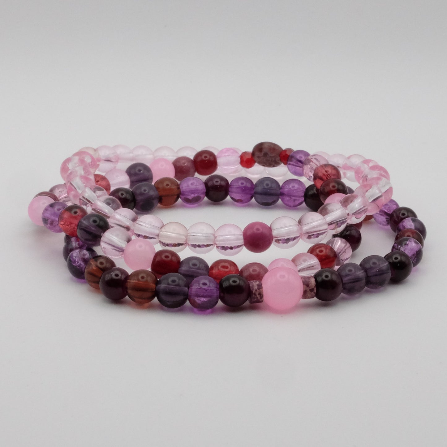 Set of three beaded bracelets in pink, purple, and red on a light gray background