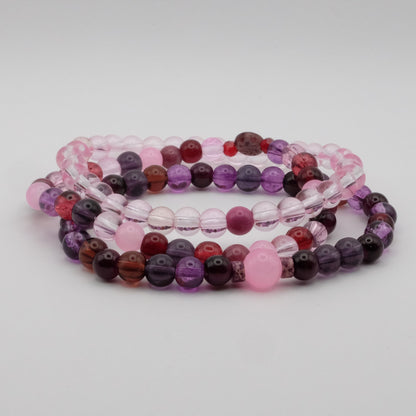 Set of three beaded bracelets in pink, purple, and red on a light gray background