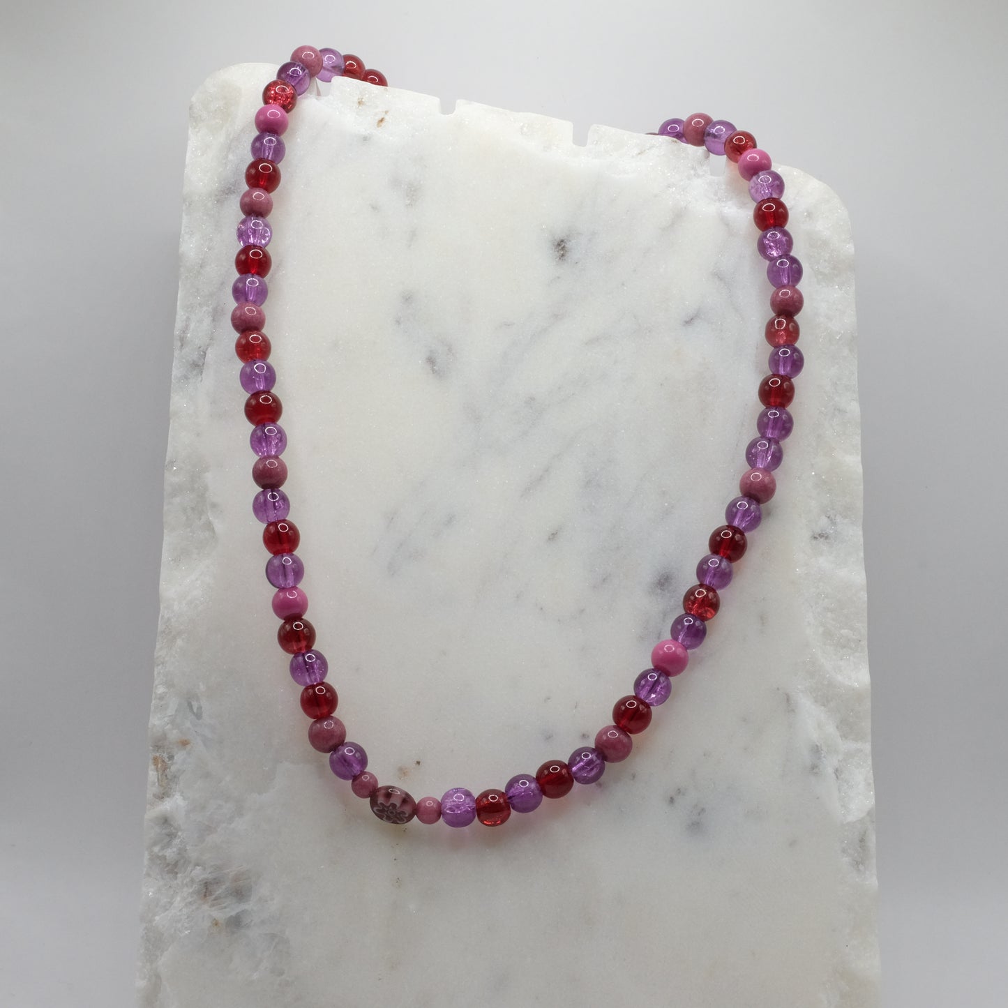 Beaded necklace with red and purple beads on a marble surface