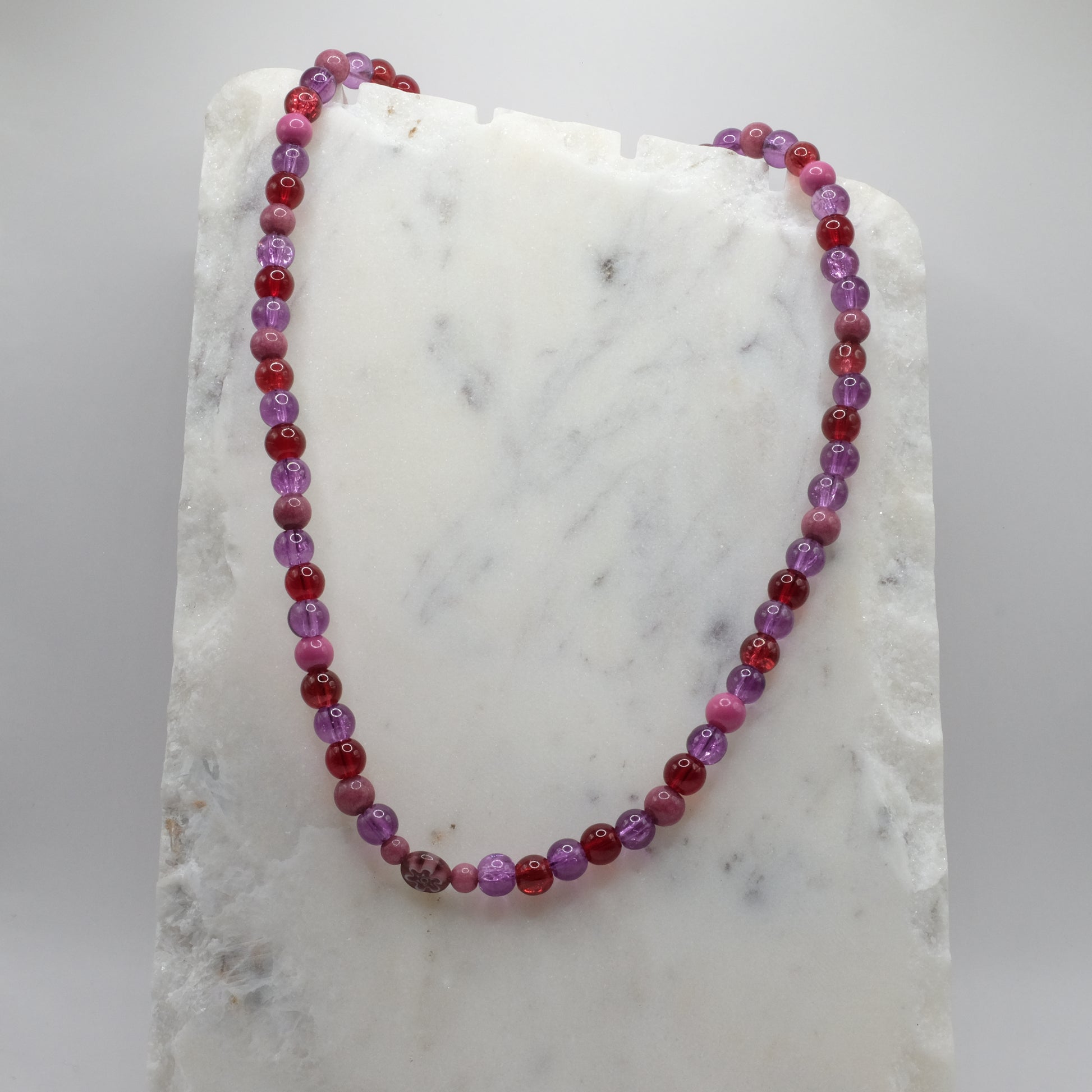 Beaded necklace with red and purple beads on a marble surface