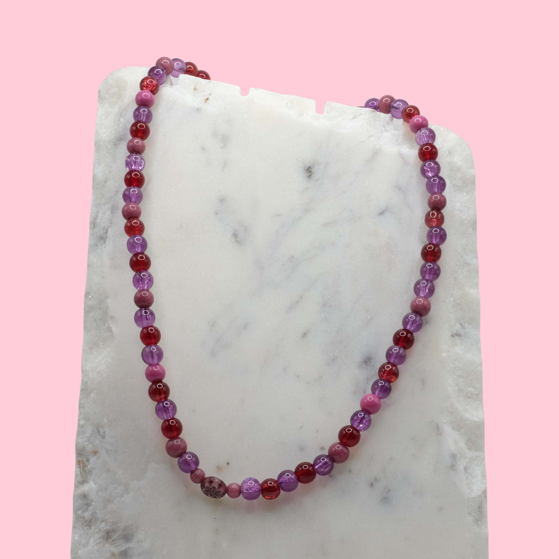 Beaded necklace with purple and red beads on a marble surface with a pink background