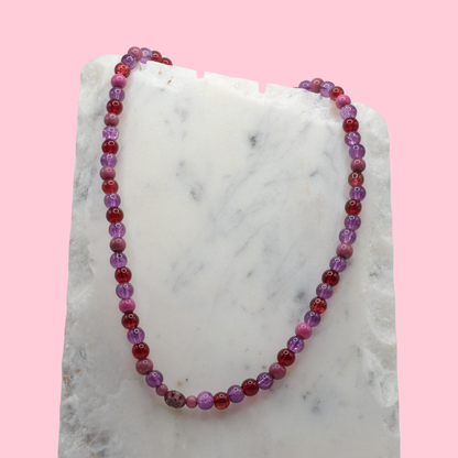 Beaded necklace with purple and red beads on a marble surface with a pink background