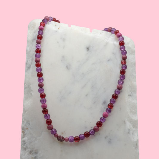 Beaded necklace with purple and red beads on a marble surface with a pink background