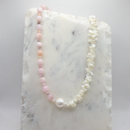 A beaded necklace composed of pink opal beads and mother of pearl chips - featuring a large freshwater pearl nugget at the centre, shown on a white marble background.