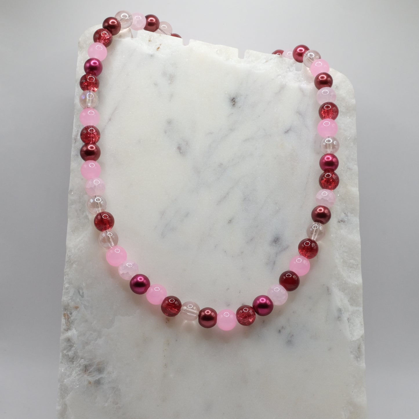 Beaded necklace with pink and red beads on a marble surface