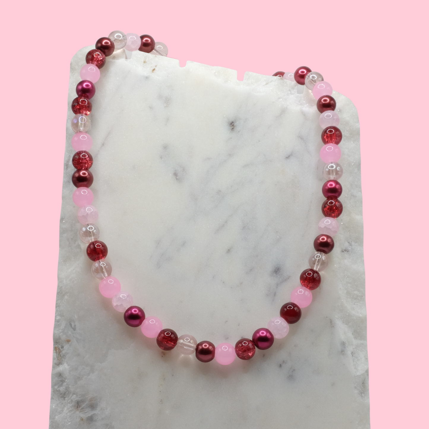 Beaded necklace with red and pink beads on a marble surface with a pink background