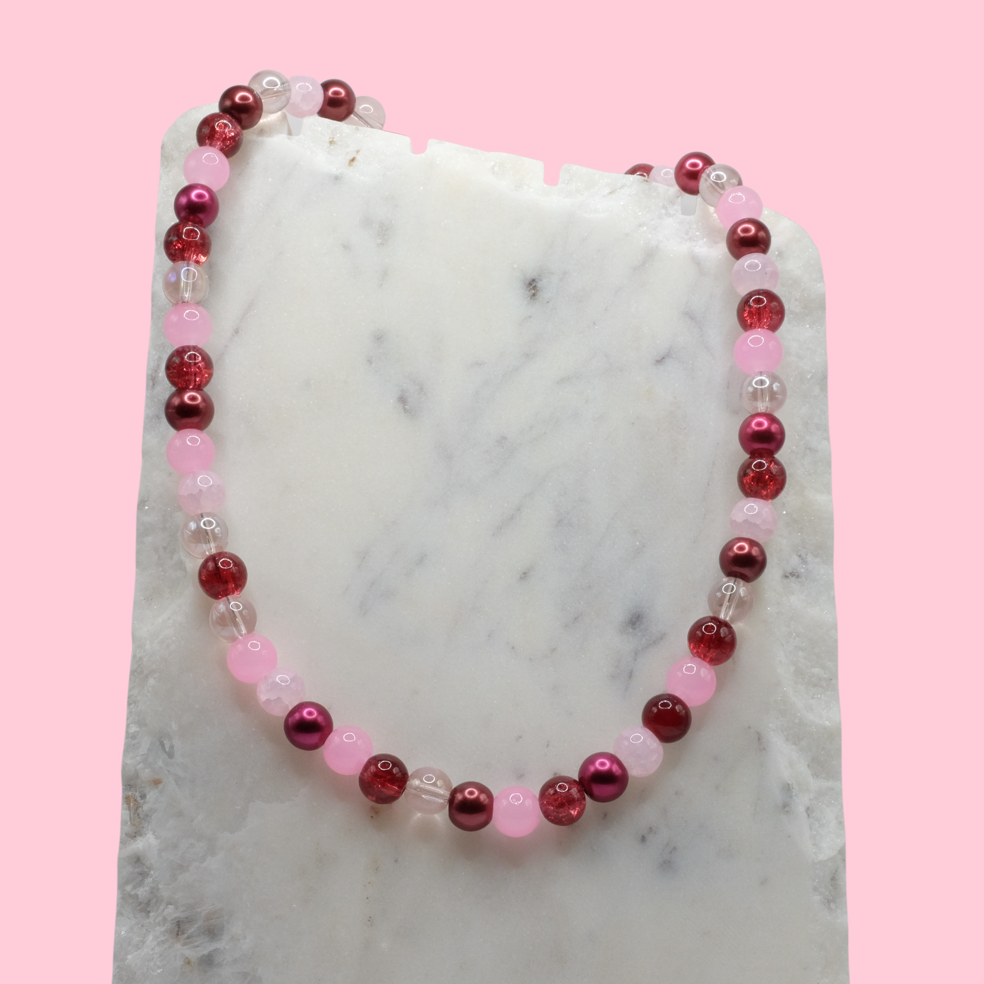 Beaded necklace with red and pink beads on a marble surface with a pink background