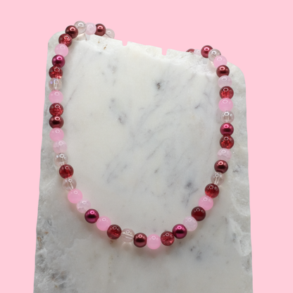Beaded necklace with red and pink beads on a marble surface with a pink background