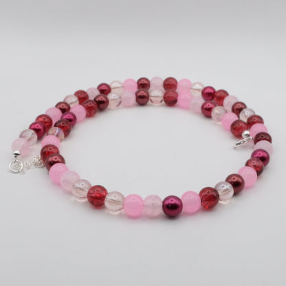 A handmade beaded necklace composed of 8mm glass beads in pink, red and plum tones featuring frosted, metallic, crackle and translucent finishes, displayed on a white background.