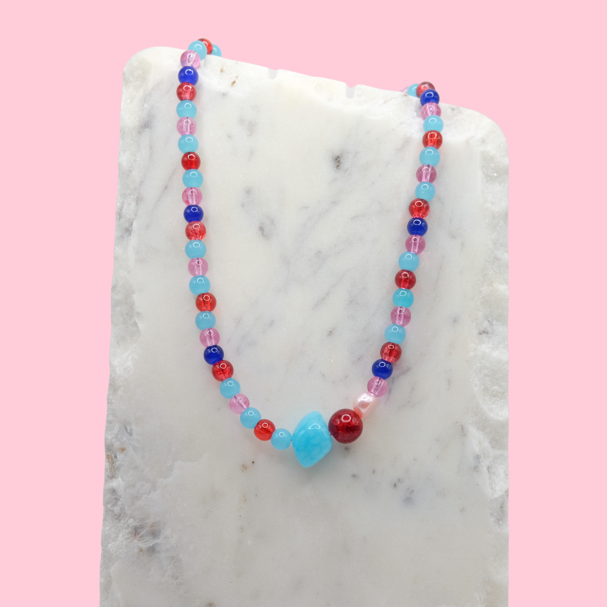 Colorful beaded necklace on a marble surface with a pink background