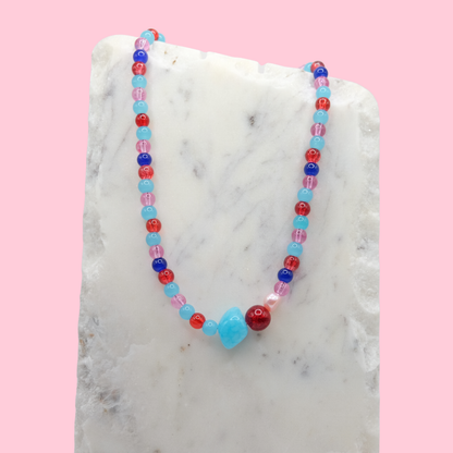 Colorful beaded necklace on a marble surface with a pink background