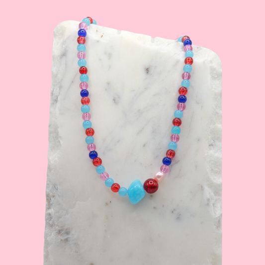 Colorful beaded necklace on a marble surface with a pink background